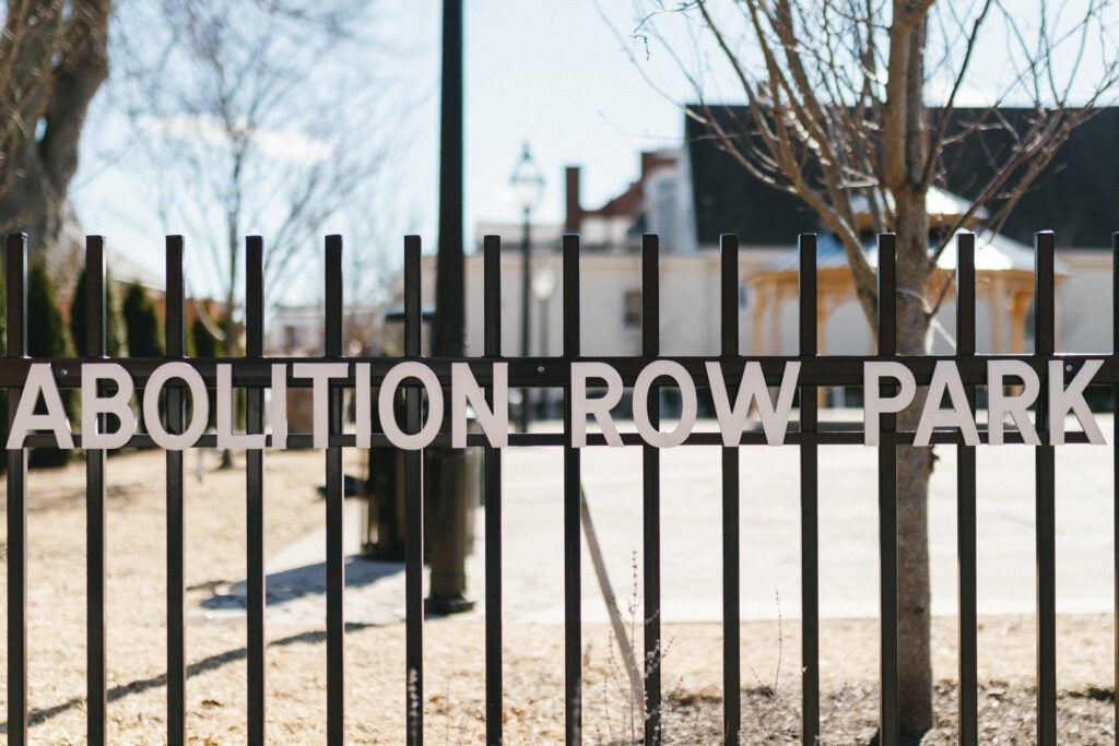 A picture of a sign on a fence that says Abolition Row Park. This sign is located in the park established by the New Bedford Historical Society in New Bedford, Massachusetts.