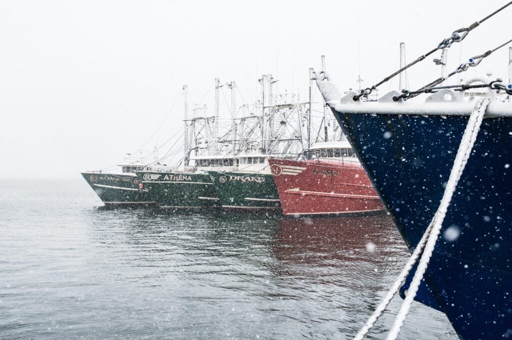 Snow falls over the New Bedford Seaport with fishing boats anchored to moorings. 